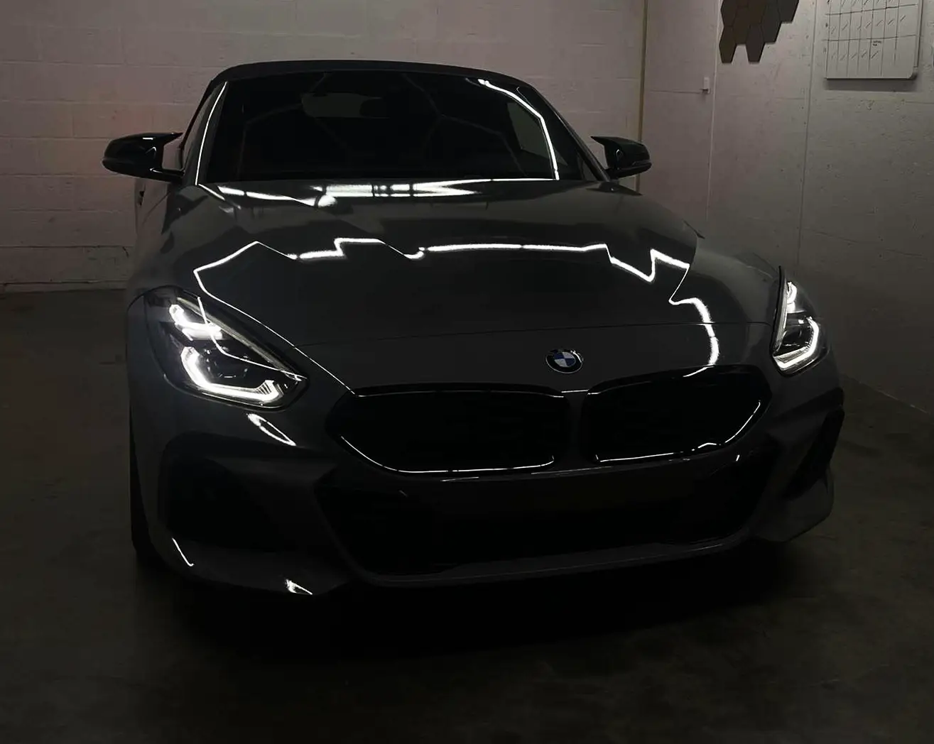Front van een BMW Z4 in glanzend grijze wrap met PPF en zwarte spiegelkappen in het atelier